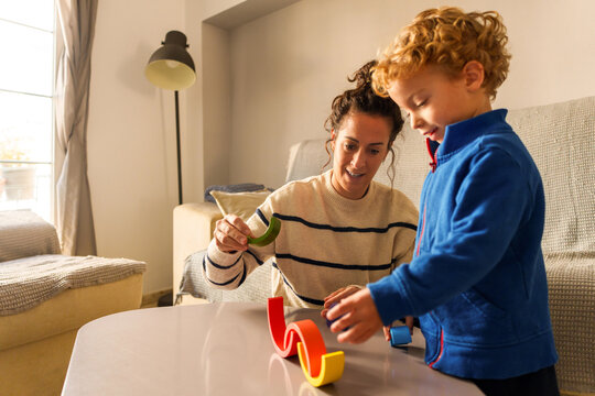 Mother and young son building a structure with colorful wooden toy pieces on a table, sharing a moment of playful learning