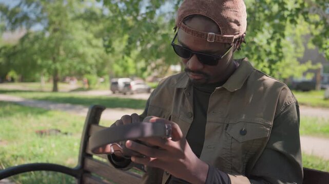 Close up of man examining and putting on over ear headphones while seated outdoors. man inspects device closely adjusting its strap before wearing it with focused attention. Bright daylight