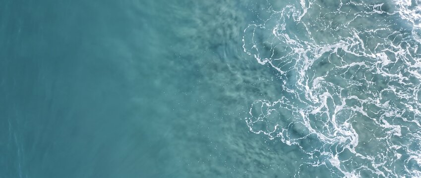 Aerial view of turquoise ocean waves crashing on the shore with white sea foam texture