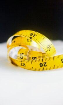coiled, bright yellow flexible measuring tape with printed black measurement markings, set against a dark, contrasting background