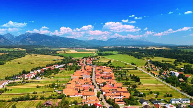Village view in the countryside. A village with red roofs sits among green fields under a blue sky. Mountains are visible in the distance.