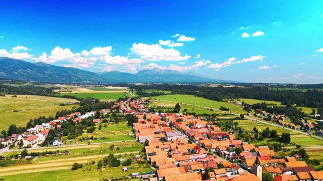 Red roof village with mountain background. Rows of houses with orange roofs stretch across a green valley below mountains.