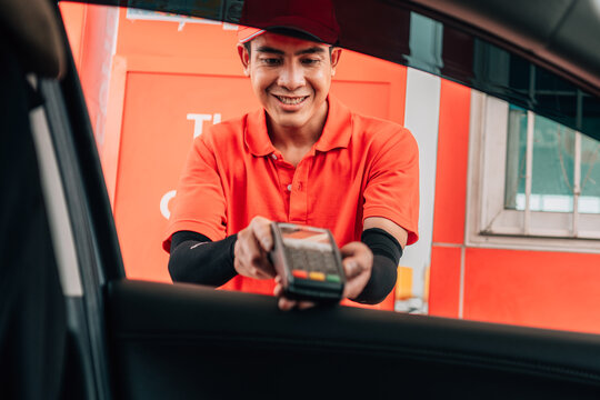 Smiling gas station attendant offering a wireless POS terminal through a car window for cashless payment.