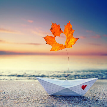 Handmade Paper Boat with Colorful Autumn Leaf on a Baltic Sea Beach at Sunset