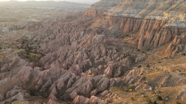 Cinematic aerial drone footage of Cappadocia&rsquo;s spectacular rock formations and fairy chimneys at sunset, bathed in warm golden light, showcasing the unique volcanic landscape of central Turkey.