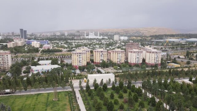 Aerial drone view over Dushanbe, Tajikistan, with residential buildings, a Ferris wheel and mosque visible against a mountainous landscape