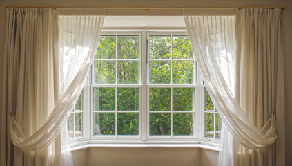 Fototapeta premium Bright window with sheer curtains framing a lush green garden view