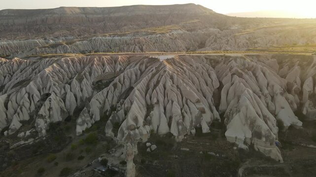 Cinematic aerial drone footage of Cappadocia&rsquo;s spectacular rock formations and fairy chimneys at sunset, bathed in warm golden light, showcasing the unique volcanic landscape of central Turkey.