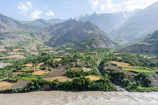 Mountain valley village in Afghanistan with terraced fields and river under snowcapped peaks