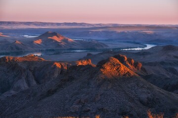 Naklejka premium High-angle view of the Ili River winding through rocky canyon and desert mountains at sunset in Kazakhstan, ideal for travel websites, geographical backgrounds, and eco-tourism banners.