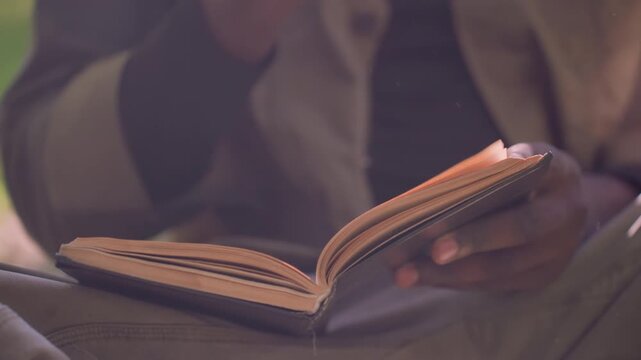 Close up of person reading open book with their hands visible focusing on interaction between fingers and pages. scene shows consistent soft lighting highlighting paper texture details