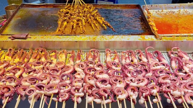 Korean Street Food &ndash; Grilling Octopus Skewers on Hot Griddle with Spicy Glaze at Night Market Stall