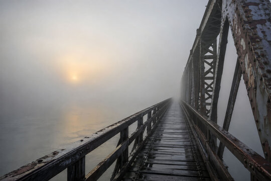 Old steel truss bridge disappearing into fog at sunrise