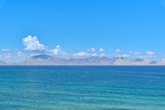 Scenic Mediterranean Sea with crystal clear turquoise water and distant rugged mountains beneath a beautiful blue sky with soft clouds on a sunny summer day