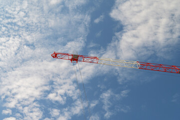 Construction crane boom against a bright blue sky with white clouds © dimas830