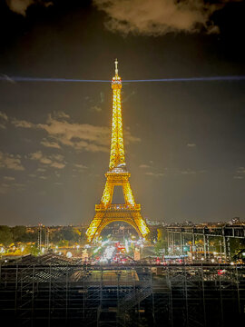 Eiffel Tower illuminated in brilliant golden lights at night with a rotating searchlight beam and the glowing Paris cityscape in the background