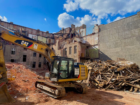 Yellow CAT excavator operating at active urban building demolition site surrounded by rubble, debris piles, and partially collapsed brick structures under blue sky