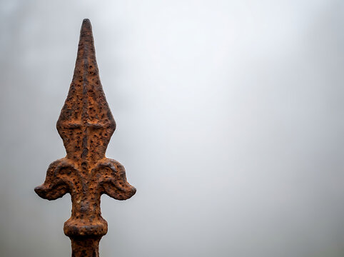 Antique rusted wrought iron spearhead fence top finial against a blurry foggy background