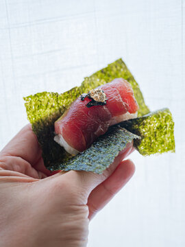 Close up of person holding delicious fresh maguro tuna sushi nori wrap fine dining omakase style.