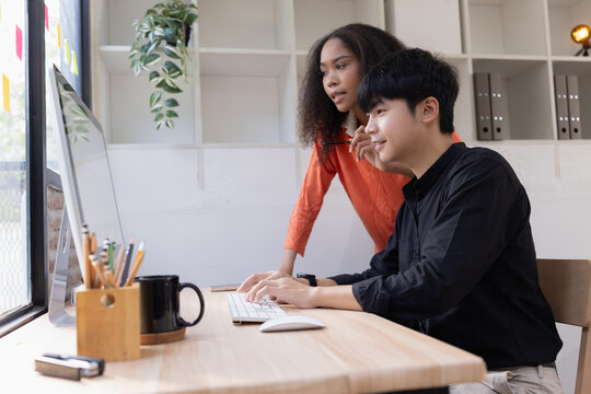A diverse young multi-ethnic creative team collaborating together in a modern office, working on a computer and discussing a project.