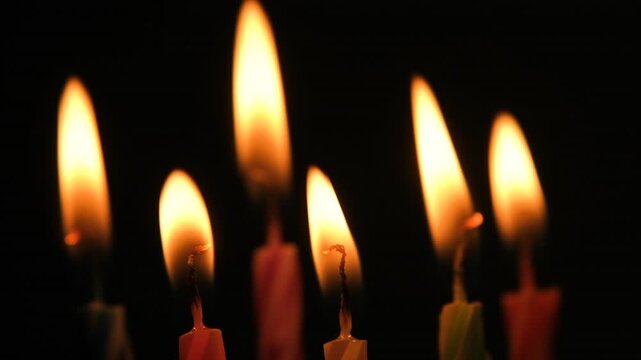 Birthday candles burning brightly against a black background before extinguishing one by one with glowing wicks and fading smoke in darkness. Slow motion