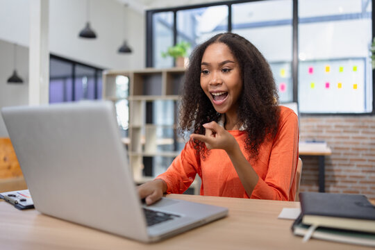 A cheerful young African American woman celebrating success while working on a laptop at her office desk.