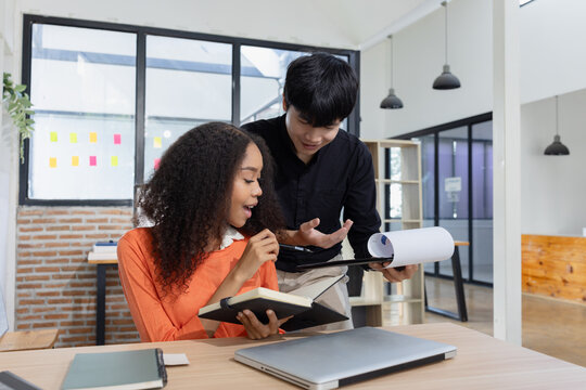 A young multiethnic male and female colleagues working together, reviewing notes and discussing business projects in a modern office.