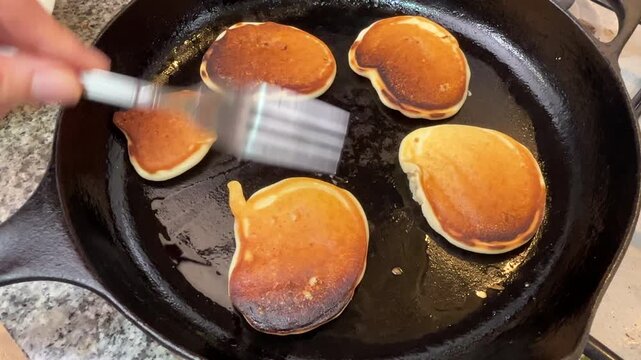 Cooking fluffy homemade pancakes in a hot cast iron skillet, flipping golden brown pancakes with a fork during preparation.