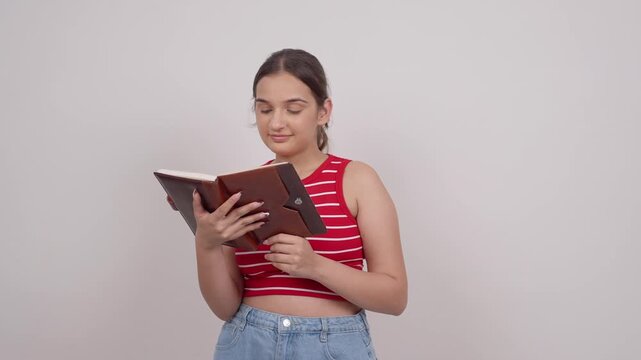 Happy Indian Teenage Girl Opening Notebook and Reading with a Smile