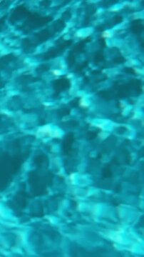Abstract turquoise swimming pool water surface with gentle ripples, shimmering sunlight reflections, and moving wave patterns.