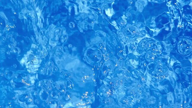 Clear blue swimming pool water surface with moving ripples, waves, reflections, and shimmering sunlight patterns.