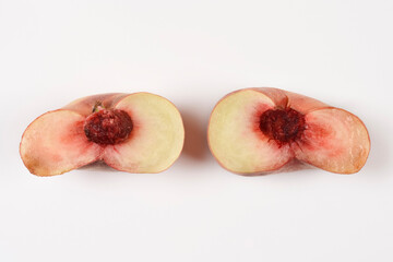 A high angle side view of a ripe flat saturn peach cut into two halves showing its inner stone and white flesh on a plain white surface. © nahhan