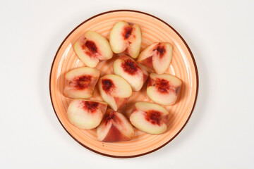 A top view of ripe flat saturn peach slices arranged on a colorful round ceramic plate placed on a plain white surface. © nahhan