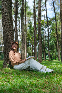 Vertical portrait image of a woman reading a book while sitting in the park