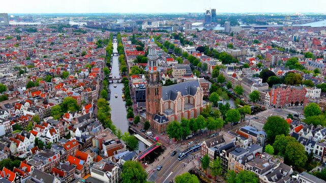 Aerial drone orbit view of the Westerkerk church tower with a tram on Rozengracht, the Prinsengracht canal running toward the IJ harbor, Amsterdam, Netherlands, in summer.