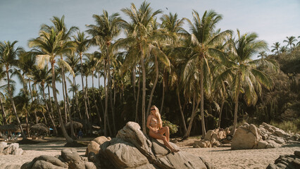Blonde Woman Sitting on Coastal Rock Formation in Front of Palm Grove © The Nomad Nextdoor