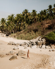 Woman Walking on Sandy Tropical Beach with Palm Trees and Large Boulders © The Nomad Nextdoor