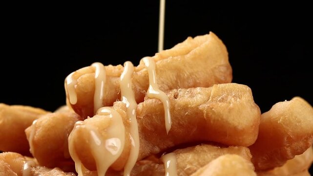 Drizzling sweetened condensed milk over fried dough sticks or chinese cruller on a black background, snack and vegan food.