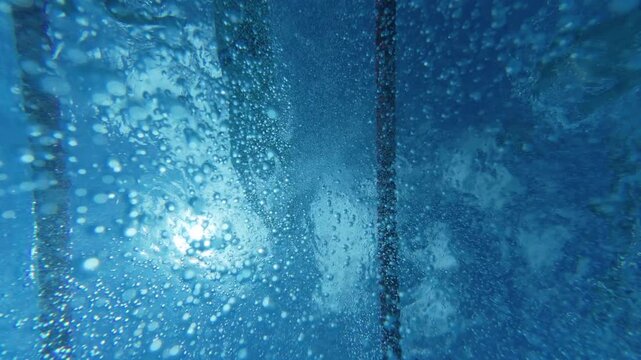 Underwater view of swimmers silhouettes and air bubbles in pool