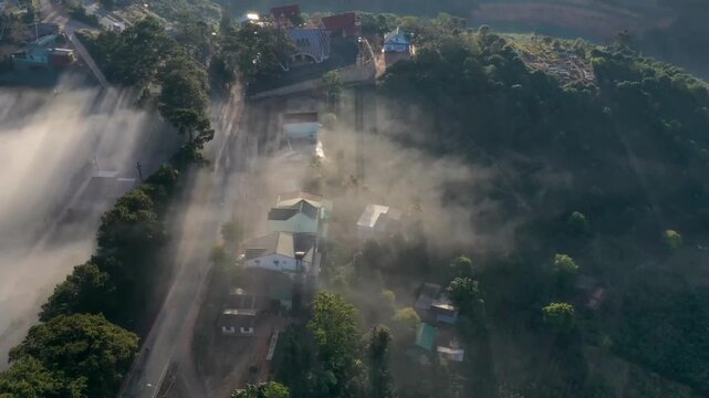 Aerial sunrise over Trai Mat, Xuan Truong Ward, Da Lat, Lam Dong, Vietnam, with drifting mist, clouds and golden sunlight illuminating the peaceful highland landscape.