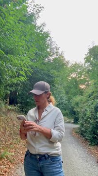 Caucasian woman in casual clothing standing on a secluded trail in the woods, trying to find a better mobile signal by raising her smartphone in the air to reconnect to the network