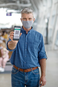 A man wearing a face mask holds up his mobile phone displaying a digital health pass or vaccination record with a QR code