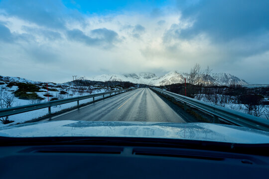 Beautiful scenic winter landscape of an empty asphalt road winding past majestic snow-covered mountains and a frozen fjord in Lofoten, Norway. Concept of adventure and freedom on an Arctic Scandinavia