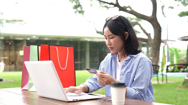 Asian woman shopping online with a laptop and credit card, surrounded by shopping bags, representing e-commerce, online payment, retail, and modern consumer lifestyle.