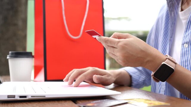 Asian woman shopping online with a laptop and credit card, surrounded by shopping bags, representing e-commerce, online payment, retail, and modern consumer lifestyle.
