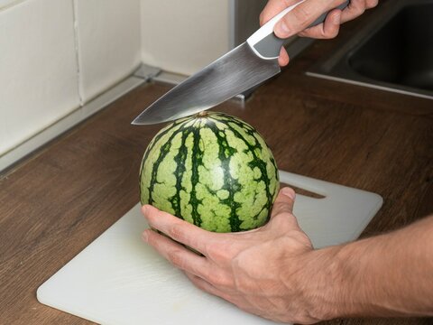 Person cutting a small watermelon on a cutting board