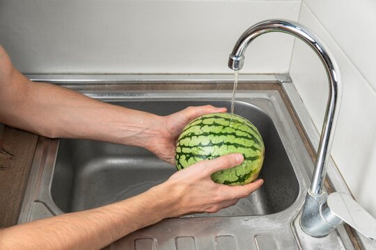 Person washing a small watermelon under running water