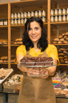 Woman baker holding fresh chocolate muffins in bakery