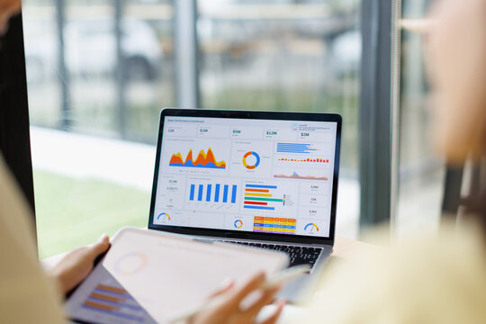 Business professionals analyzing financial data dashboard on a laptop and tablet, working together on market research and sales performance analytics