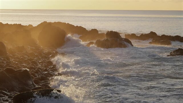 Powerful Atlantic ocean waves crashing on the rocky volcanic coast of Madeira island during warm golden hour sunset with glowing sea spray and cinematic mist. 4K video.